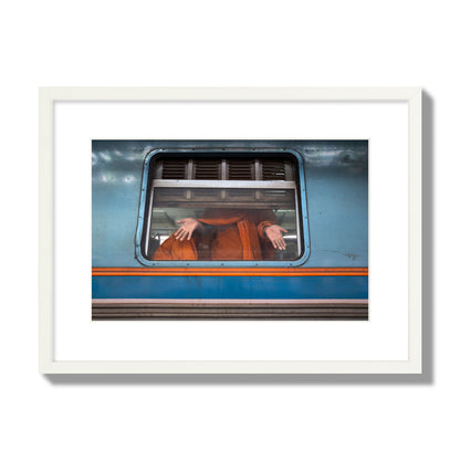 Fine art photograph of a Buddhist monk standing with open hands at a train car window. Archival pigment print, medium size, white frame.