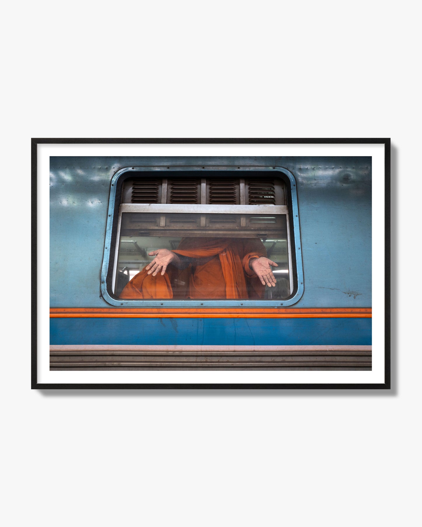 Fine art photograph of a Buddhist monk standing with open hands at a train car window. Archival pigment print, black frame.