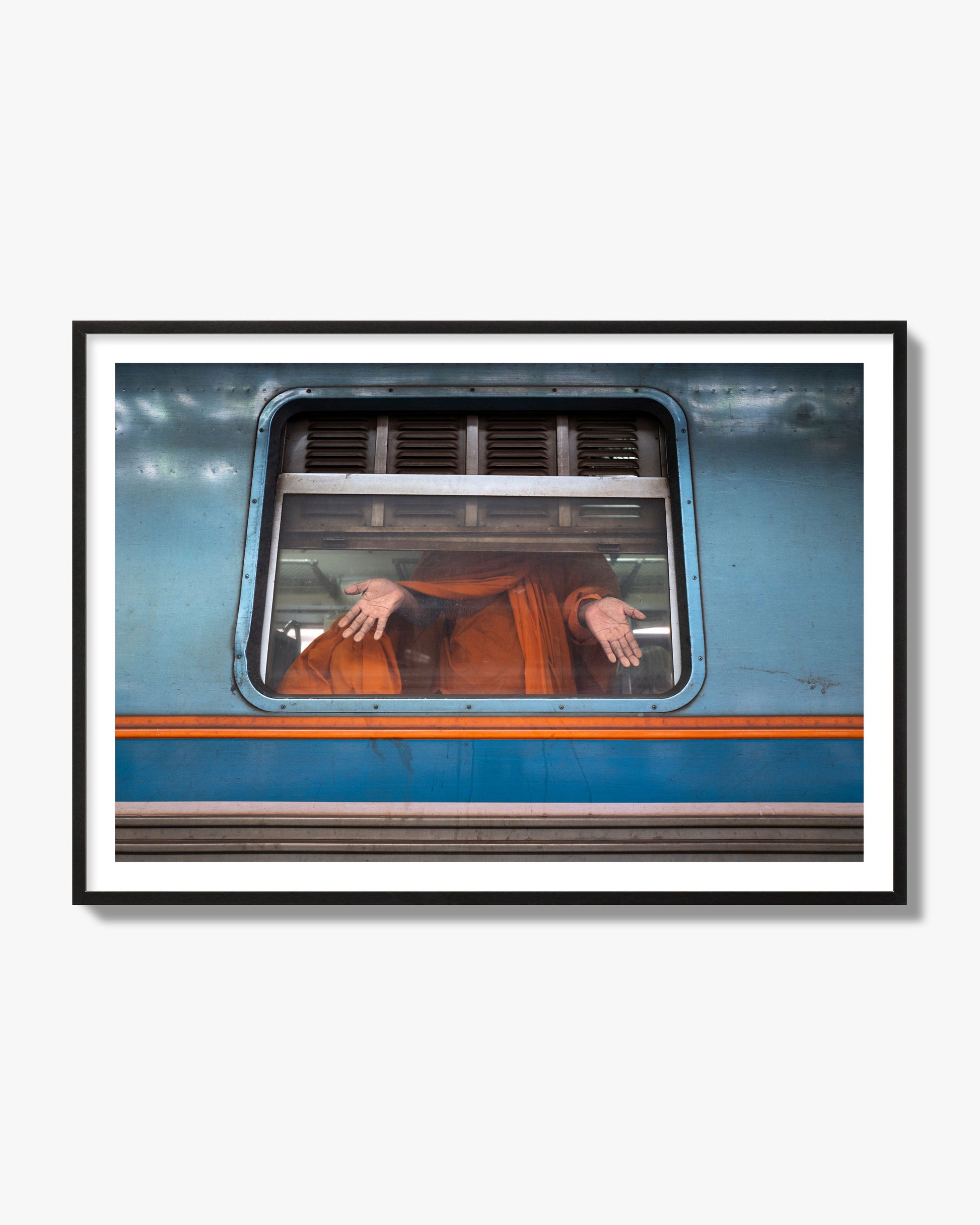 Fine art photograph of a Buddhist monk standing with open hands at a train car window. Archival pigment print, black frame.