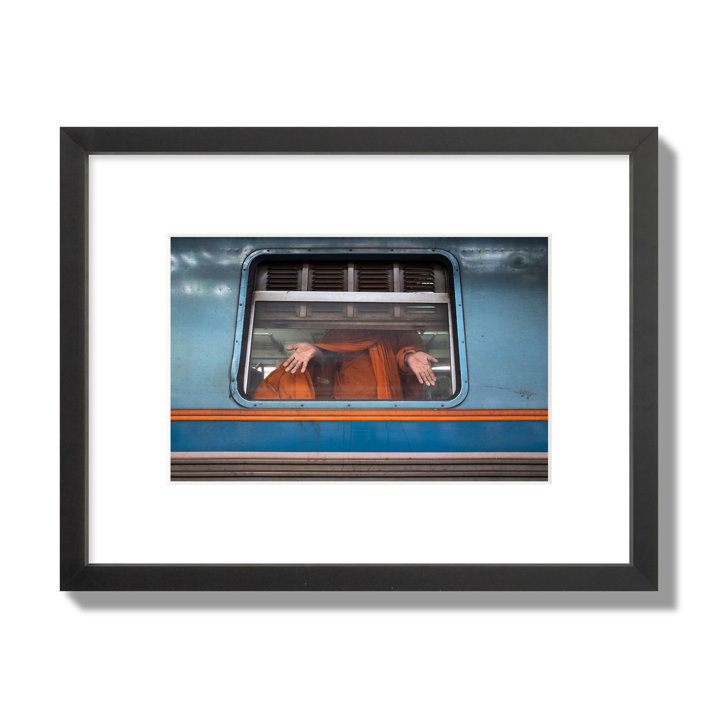 Fine art photograph of a Buddhist monk standing with open hands at a train car window. Archival pigment print, small size, black frame.