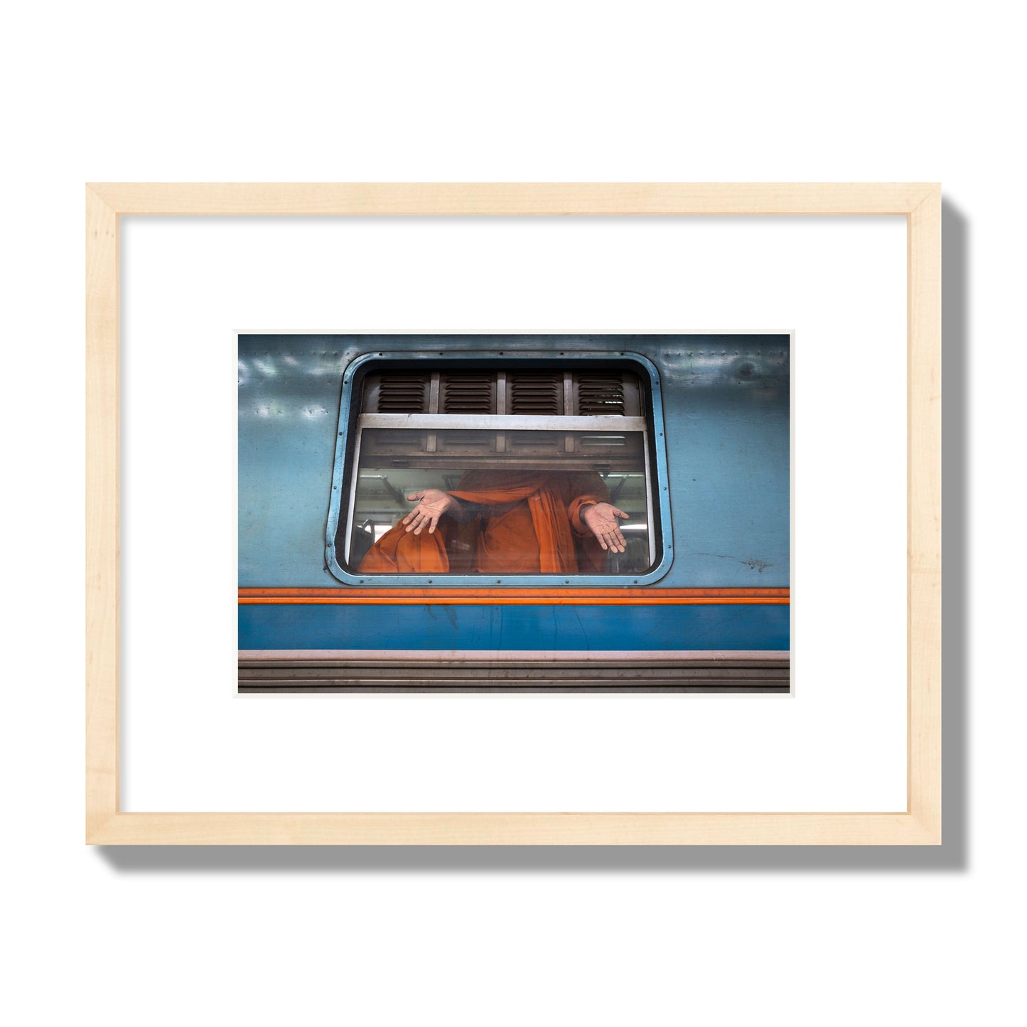 Fine art photograph of a Buddhist monk standing with open hands at a train car window. Archival pigment print, small size, natural wood frame.