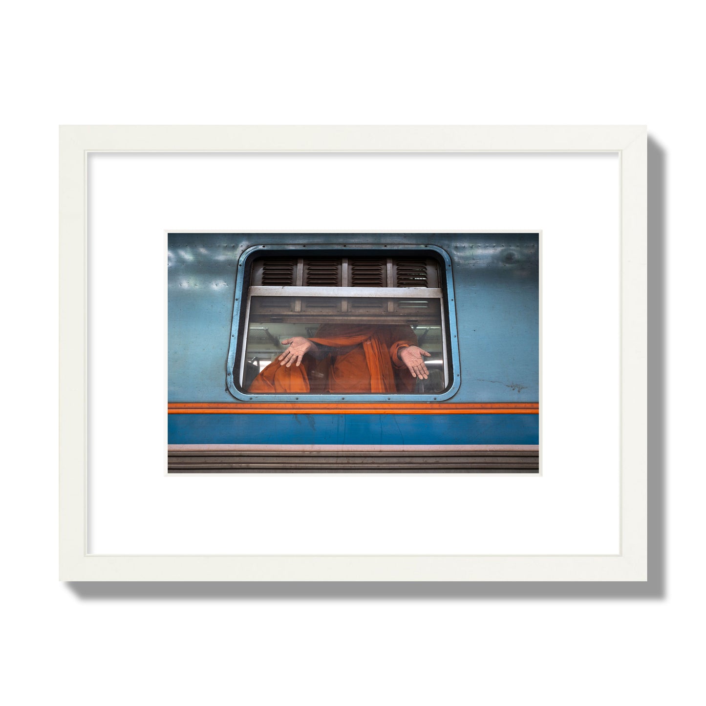 Fine art photograph of a Buddhist monk standing with open hands at a train car window. Archival pigment print, small size, white frame.