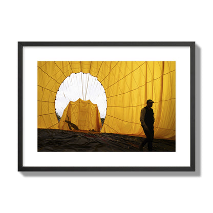Fine art photograph of a man walking inside a bright yellow hot air balloon as it slowly deflates. Archival pigment print, large size, black frame.