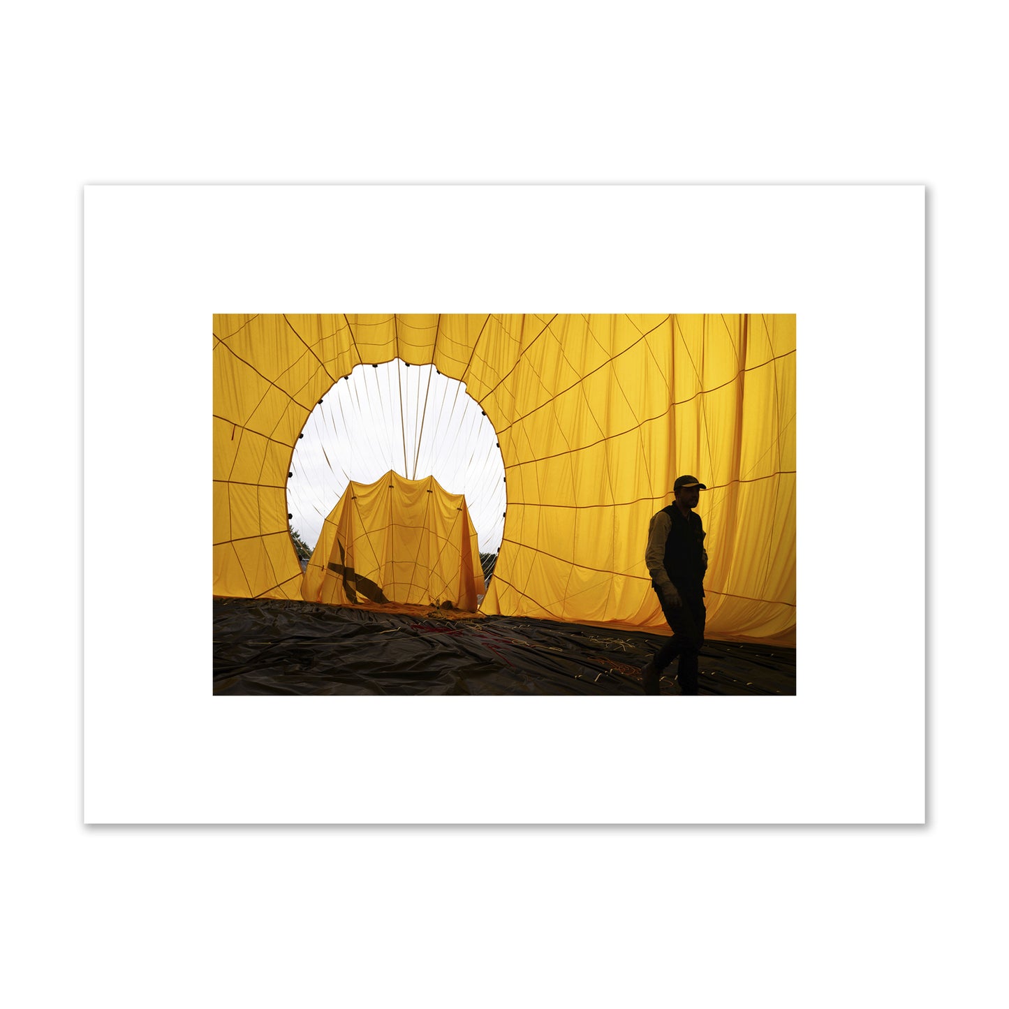 Fine art photograph of a man walking inside a bright yellow hot air balloon as it slowly deflates. Archival pigment print, small size, unframed.