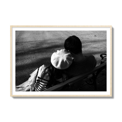 Fine art black and white street photograph of a romantic couple cuddling on a park bench. Archival pigment print, collector size, natural wood frame.