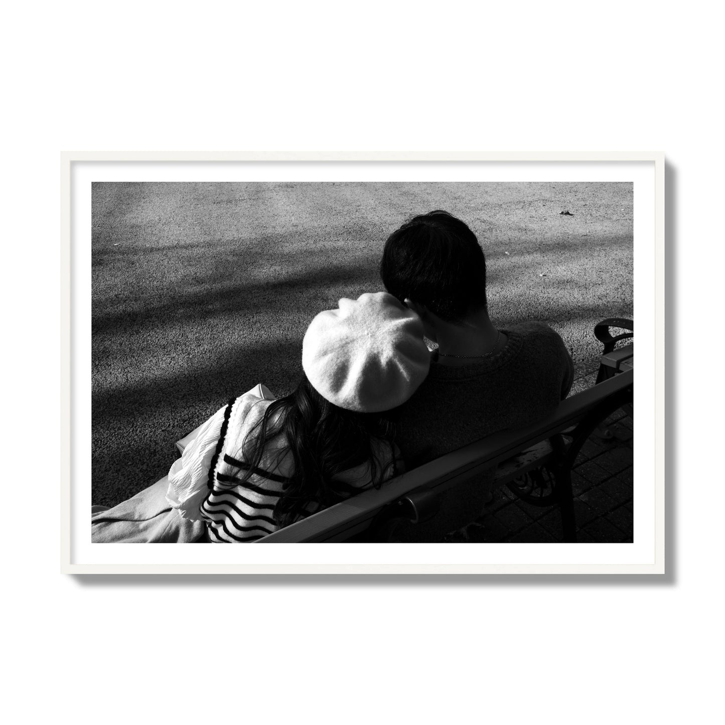 Fine art black and white street photograph of a romantic couple cuddling on a park bench. Archival pigment print, collector size, white frame.