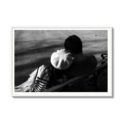 Fine art black and white street photograph of a romantic couple cuddling on a park bench. Archival pigment print, gallery size, white frame.