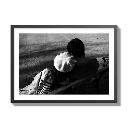 Fine art black and white street photograph of a romantic couple cuddling on a park bench. Archival pigment print, giant size, black frame.