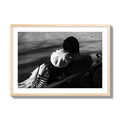 Fine art black and white street photograph of a romantic couple cuddling on a park bench. Archival pigment print, giant size, natural wood frame.