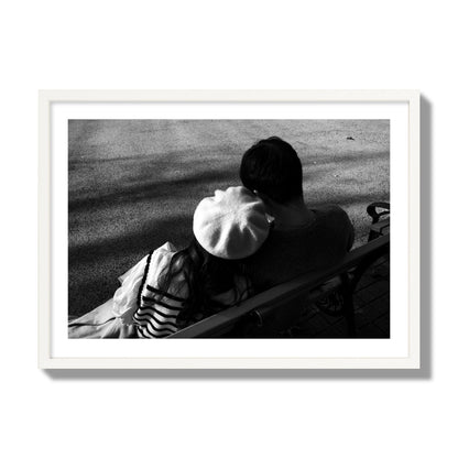 Fine art black and white street photograph of a romantic couple cuddling on a park bench. Archival pigment print, giant size, white frame.