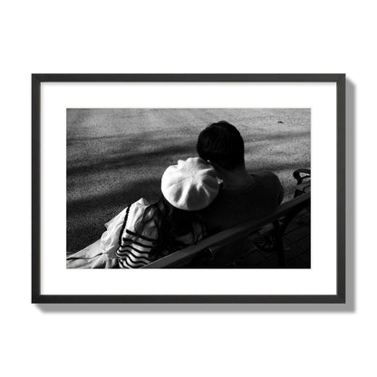Fine art black and white street photograph of a romantic couple cuddling on a park bench. Archival pigment print, large size, black frame.
