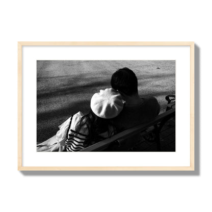Fine art black and white street photograph of a romantic couple cuddling on a park bench. Archival pigment print, large size, natural wood frame.