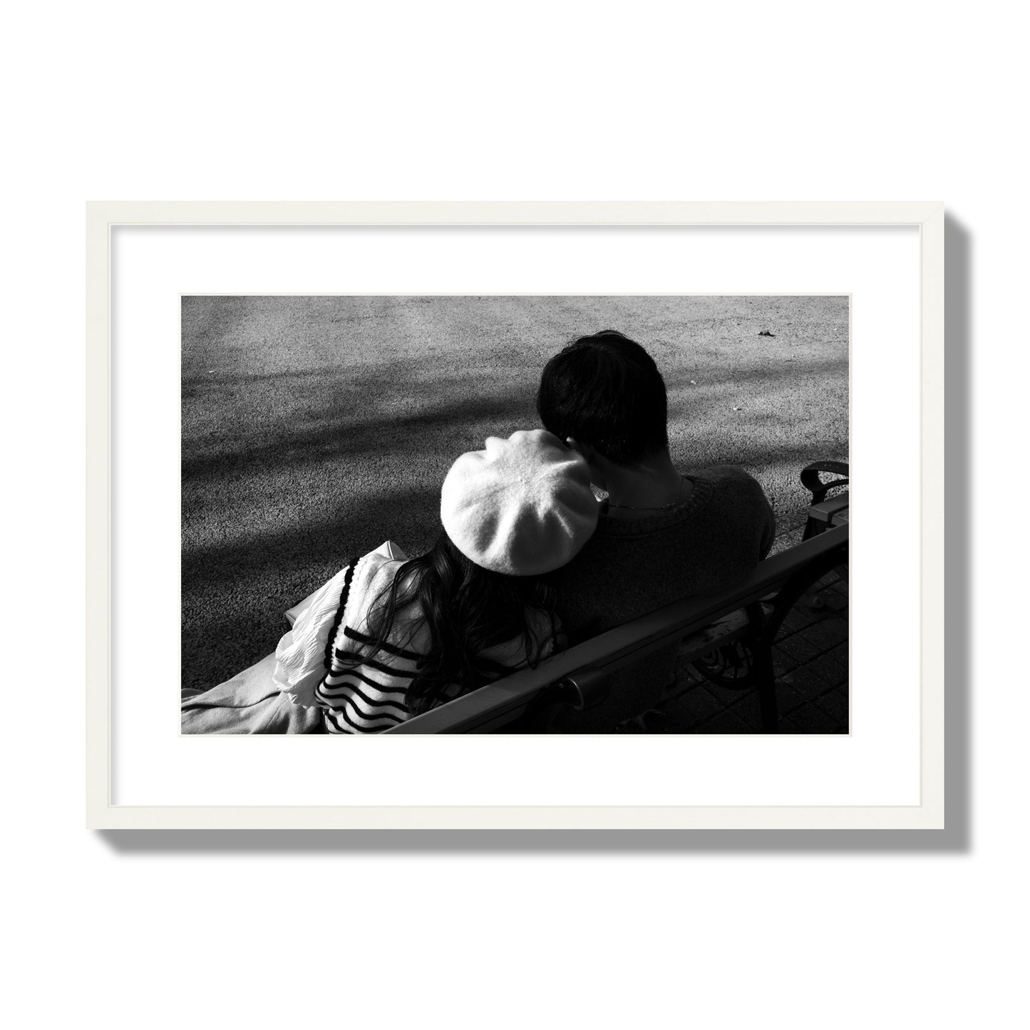 Fine art black and white street photograph of a romantic couple cuddling on a park bench. Archival pigment print, large size, white frame.