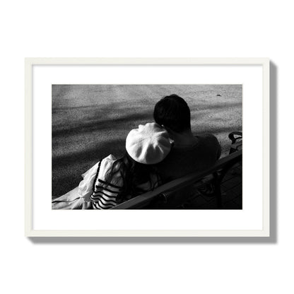 Fine art black and white street photograph of a romantic couple cuddling on a park bench. Archival pigment print, large size, white frame.