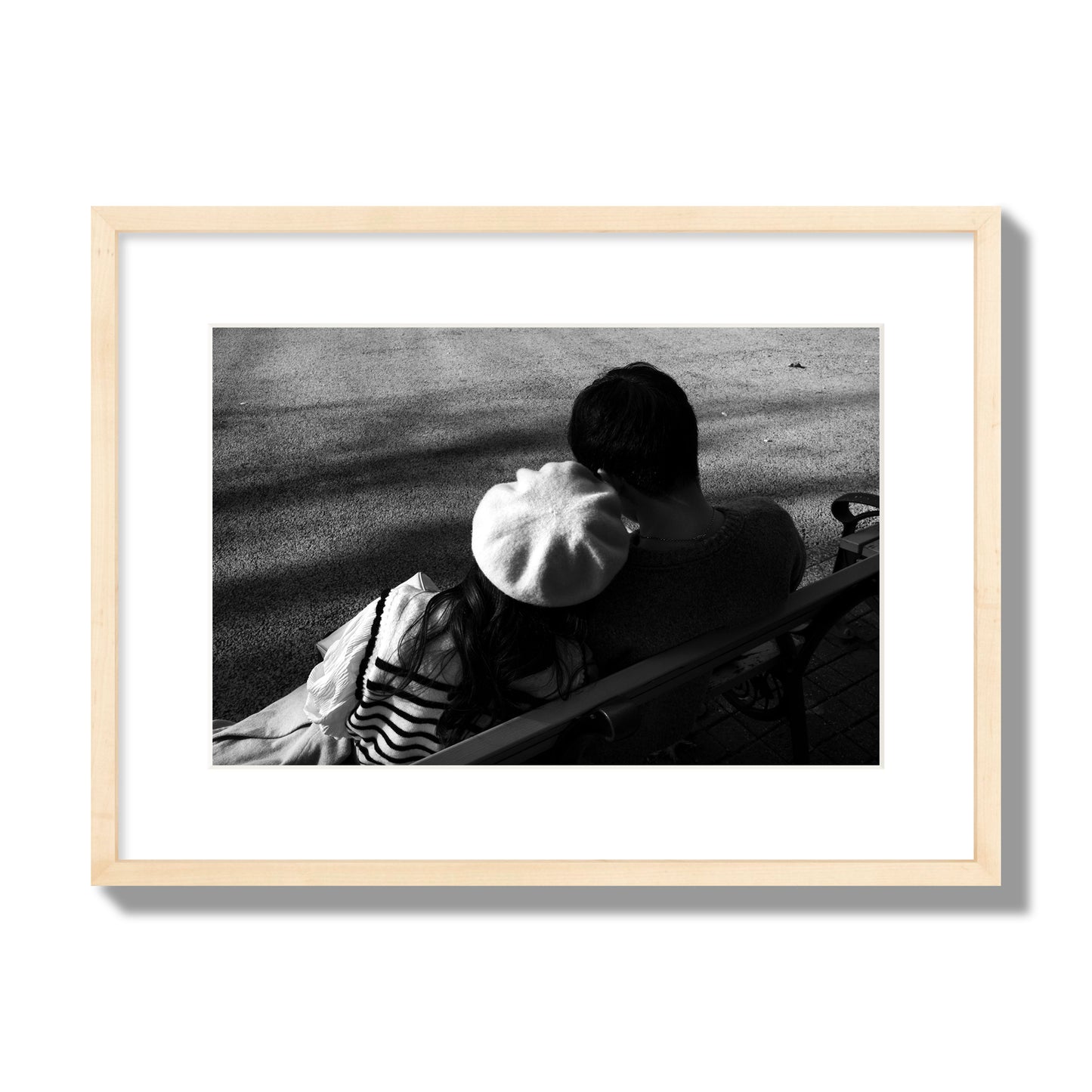 Fine art black and white street photograph of a romantic couple cuddling on a park bench. Archival pigment print, medium size, natural wood frame.