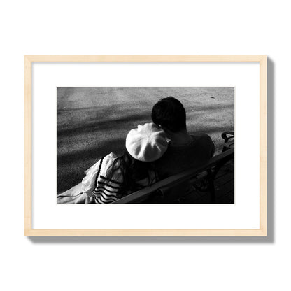 Fine art black and white street photograph of a romantic couple cuddling on a park bench. Archival pigment print, medium size, natural wood frame.