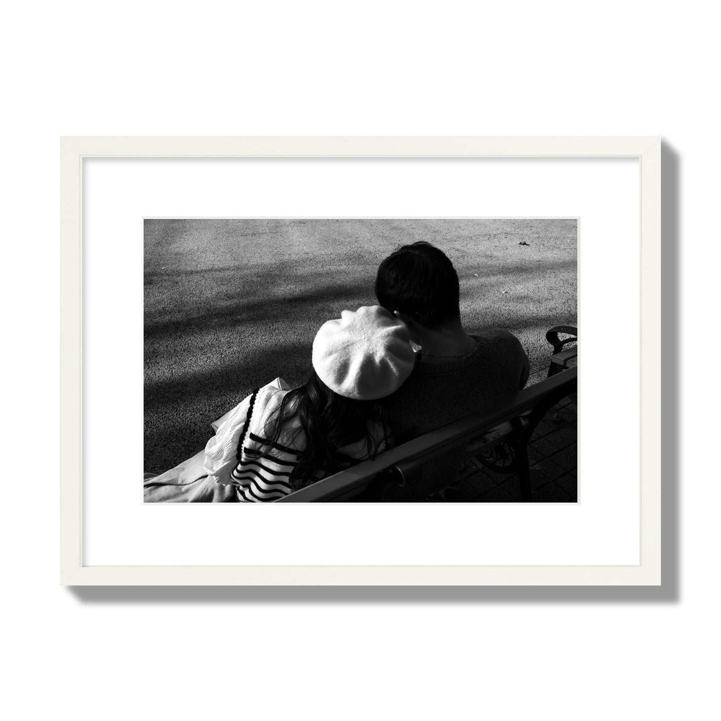 Fine art black and white street photograph of a romantic couple cuddling on a park bench. Archival pigment print, medium size, white frame.