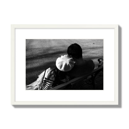 Fine art black and white street photograph of a romantic couple cuddling on a park bench. Archival pigment print, medium size, white frame.
