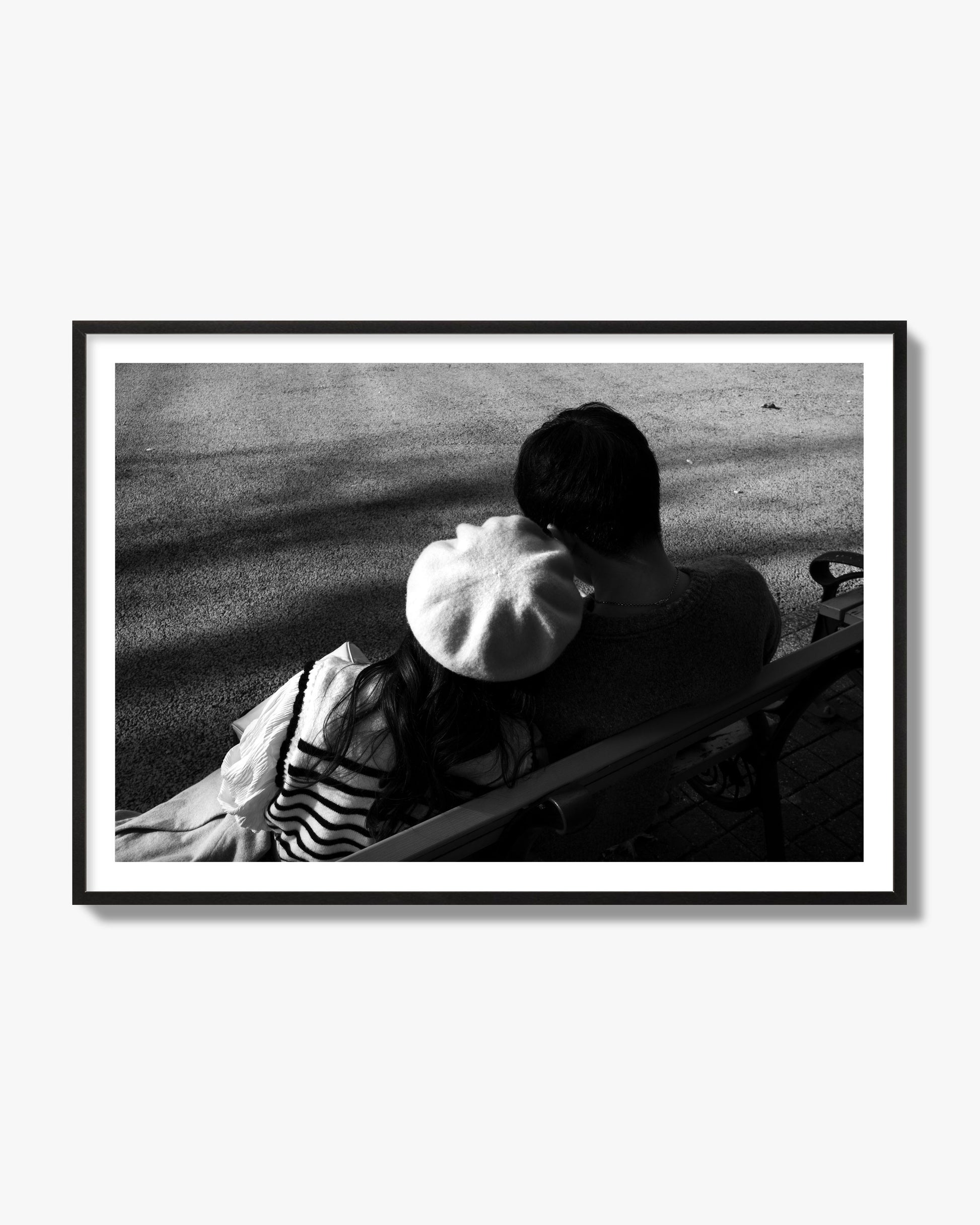 Fine art black and white street photograph of a romantic couple cuddling on a park bench. Archival pigment print, black frame.