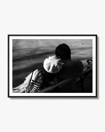 Fine art black and white street photograph of a romantic couple cuddling on a park bench. Archival pigment print, black frame.