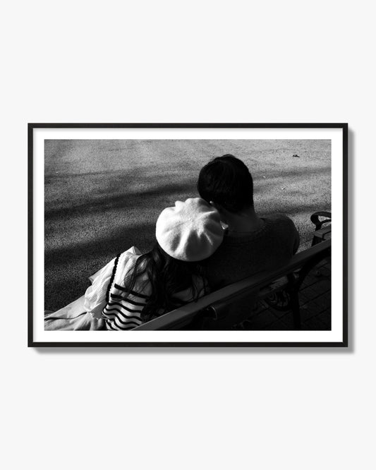 Fine art black and white street photograph of a romantic couple cuddling on a park bench. Archival pigment print, black frame.
