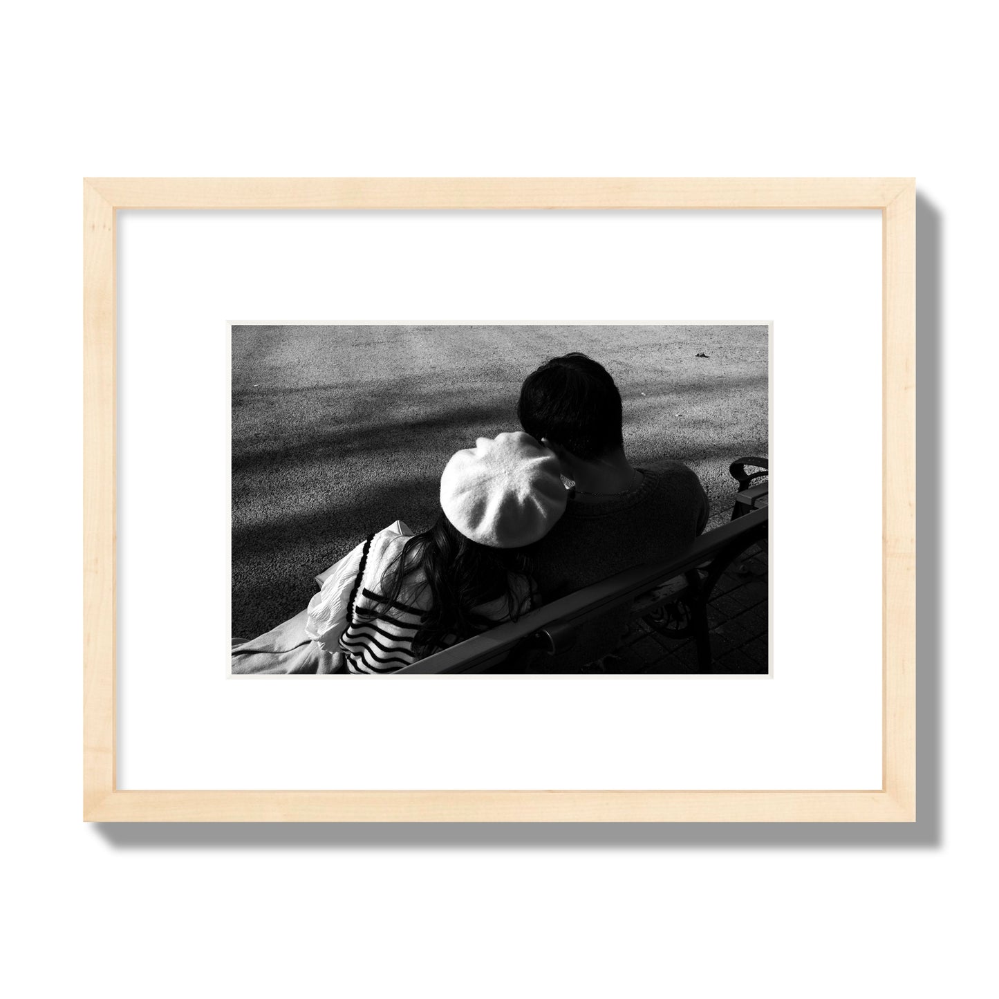 Fine art black and white street photograph of a romantic couple cuddling on a park bench. Archival pigment print, small size, natural wood frame.
