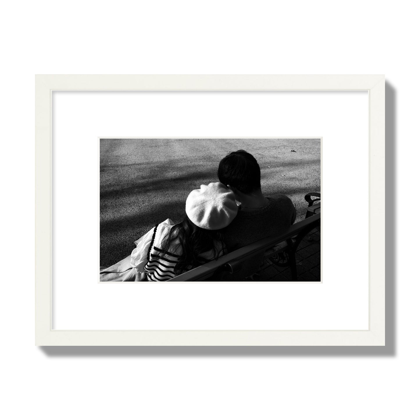 Fine art black and white street photograph of a romantic couple cuddling on a park bench. Archival pigment print, small size, white frame.