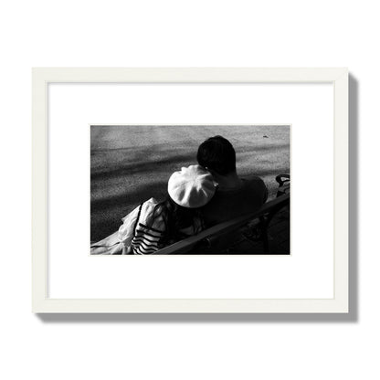 Fine art black and white street photograph of a romantic couple cuddling on a park bench. Archival pigment print, small size, white frame.