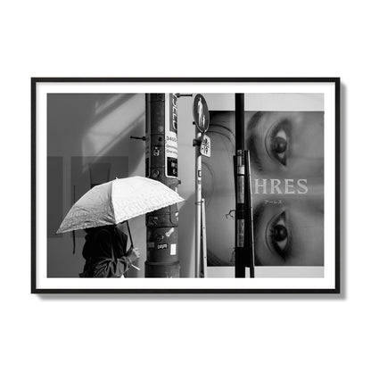 Fine art street photograph of a woman walking with an umbrella on a Tokyo street, passing beneath a billboard with two large eyes. Archival pigment print, collector size, black frame.