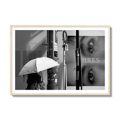 Fine art street photograph of a woman walking with an umbrella on a Tokyo street, passing beneath a billboard with two large eyes. Archival pigment print, collector size, natural wood frame.