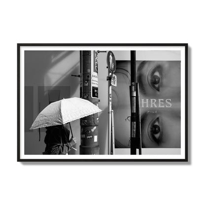 Fine art street photograph of a woman walking with an umbrella on a Tokyo street, passing beneath a billboard with two large eyes. Archival pigment print, gallery size, black frame.
