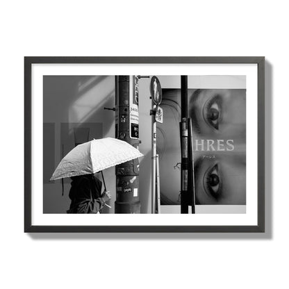 Fine art street photograph of a woman walking with an umbrella on a Tokyo street, passing beneath a billboard with two large eyes. Archival pigment print, giant size, black frame.