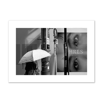 Fine art street photograph of a woman walking with an umbrella on a Tokyo street, passing beneath a billboard with two large eyes. Archival pigment print, giant size, unframed.