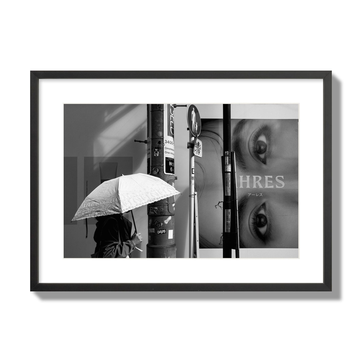 Fine art street photograph of a woman walking with an umbrella on a Tokyo street, passing beneath a billboard with two large eyes. Archival pigment print, large size, black frame.