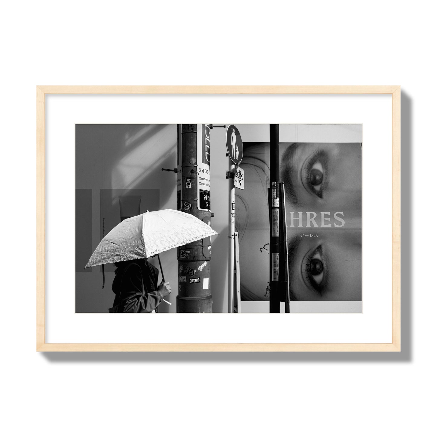 Fine art street photograph of a woman walking with an umbrella on a Tokyo street, passing beneath a billboard with two large eyes. Archival pigment print, large size, natural wood frame.
