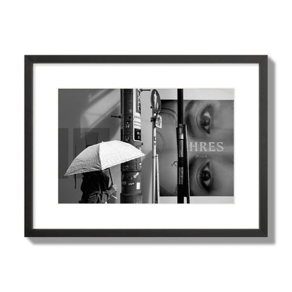 Fine art street photograph of a woman walking with an umbrella on a Tokyo street, passing beneath a billboard with two large eyes. Archival pigment print, medium size, black frame.
