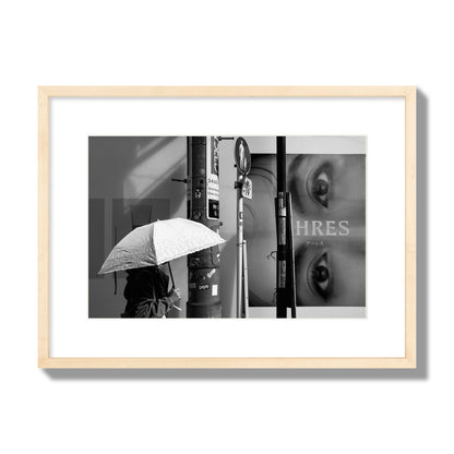 Fine art street photograph of a woman walking with an umbrella on a Tokyo street, passing beneath a billboard with two large eyes. Archival pigment print, medium size, natural wood frame.