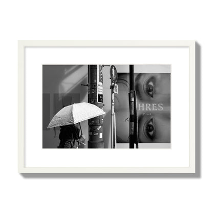 Fine art street photograph of a woman walking with an umbrella on a Tokyo street, passing beneath a billboard with two large eyes. Archival pigment print, medium size, white frame.