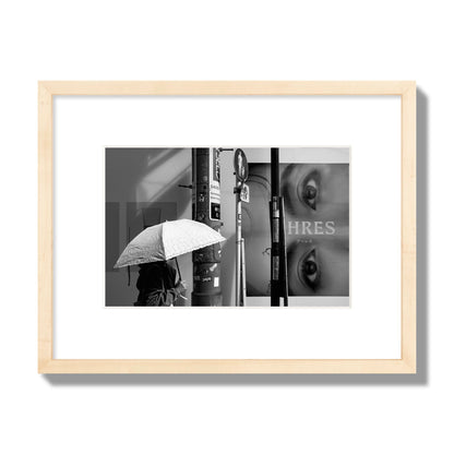 Fine art street photograph of a woman walking with an umbrella on a Tokyo street, passing beneath a billboard with two large eyes. Archival pigment print, small size, natural wood frame.
