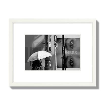 Fine art street photograph of a woman walking with an umbrella on a Tokyo street, passing beneath a billboard with two large eyes. Archival pigment print, small size, white frame.