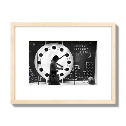 Fine art street photograph of a woman checking her watch as she walks past a giant clock on a busy Tokyo city street. Archival pigment print, small size, natural wood frame.