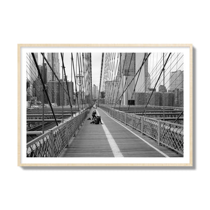 Fine art black and white photograph of a person posing on the Brooklyn Bridge with the cityscape in the background, archival pigment print, collector size, natural wood frame