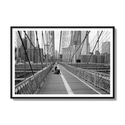 Fine art black and white photograph of a person posing on the Brooklyn Bridge with the cityscape in the background, archival pigment print, gallery size, black frame