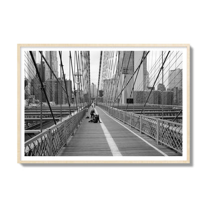 Fine art black and white photograph of a person posing on the Brooklyn Bridge with the cityscape in the background, archival pigment print, gallery size, natural wood frame