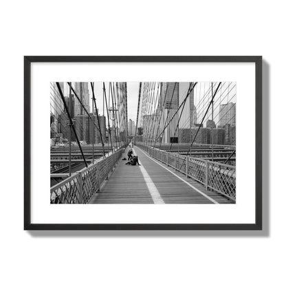 Fine art black and white photograph of a person posing on the Brooklyn Bridge with the cityscape in the background, archival pigment print, large size, black frame