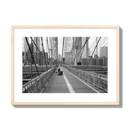 Fine art black and white photograph of a person posing on the Brooklyn Bridge with the cityscape in the background, archival pigment print, large size, natural wood frame