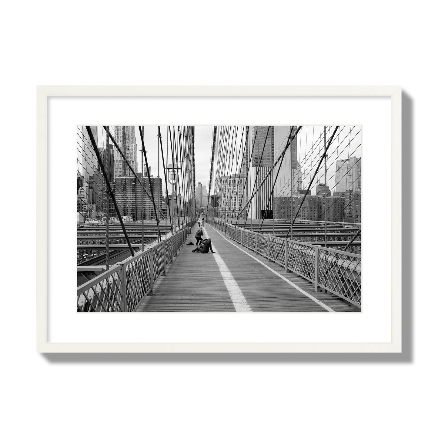 Fine art black and white photograph of a person posing on the Brooklyn Bridge with the cityscape in the background, archival pigment print, large size, white frame