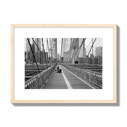 Fine art black and white photograph of a person posing on the Brooklyn Bridge with the cityscape in the background, archival pigment print, medium size, natural wood frame