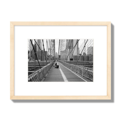 Fine art black and white photograph of a person posing on the Brooklyn Bridge with the cityscape in the background, archival pigment print, small size, natural wood frame