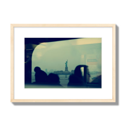 Fine art photograph of passengers silhouetted on a crowded ferry with the Statue of Liberty in the background, archival pigment print, medium size, natural wood frame.